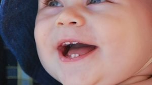 Photo of smiling baby boy with his first teeth for our article about teething symptoms