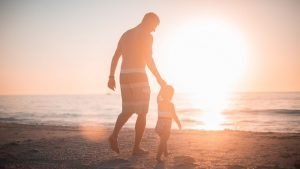 Image for our article about ideas for Father's Day. It is a picture of a dad walking on a beach with his daughter at sunset
