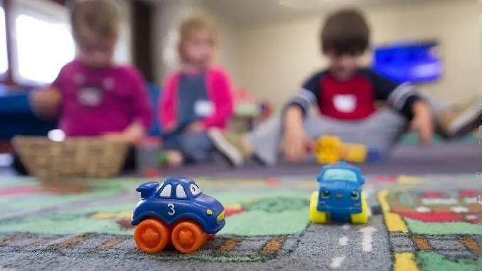 30 hours free childcare article image. Image is of 2 toy cars in the foreground and 3 children, a girl and 2 boys playing in the background, they are blurred out.