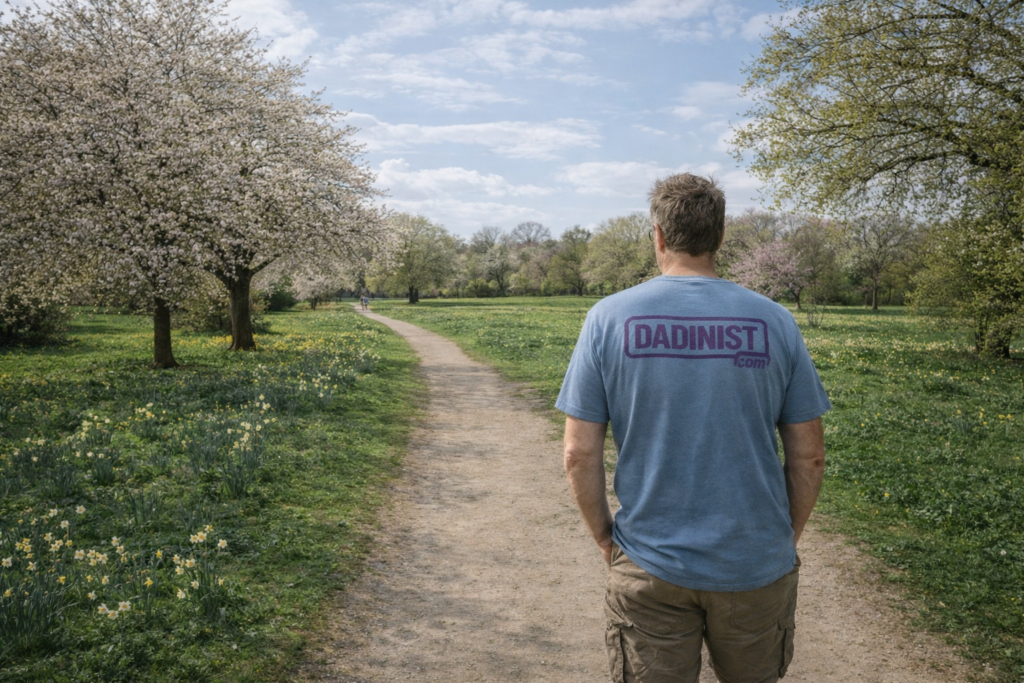 Father walking alone along a park path in spring, seen from behind and wearing a Dadinist.com t-shirt.